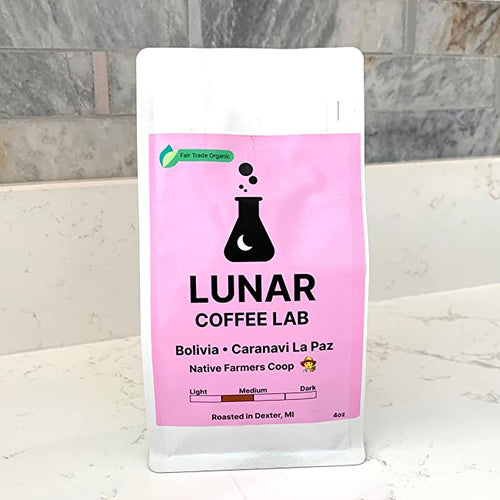 Lunar Coffee Lab Bolivia Caranavi La Paz in a white pouch with a pink label and the moon-and-flask mark, on a marble counter.