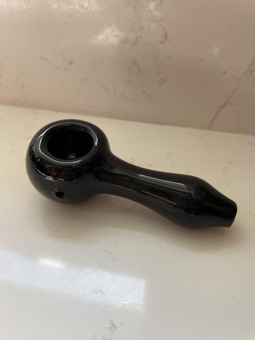 Glossy black glass spoon pipe with a polished bowl rim, resting on warm marble.