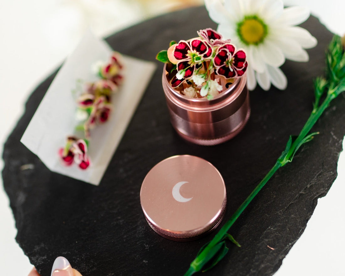 Rose gold grinder styled with pressed flowers on a slate surface