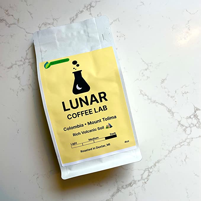 Lunar Coffee Lab Colombia Mount Tolima in a white pouch with a butter-yellow label and the moon-and-flask mark, on white marble.