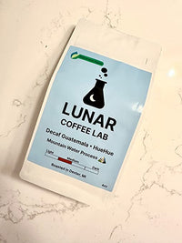 Lunar Coffee Lab Decaf Guatemala HueHue, 4oz, in a white pouch with a pale blue label, lying on white marble.