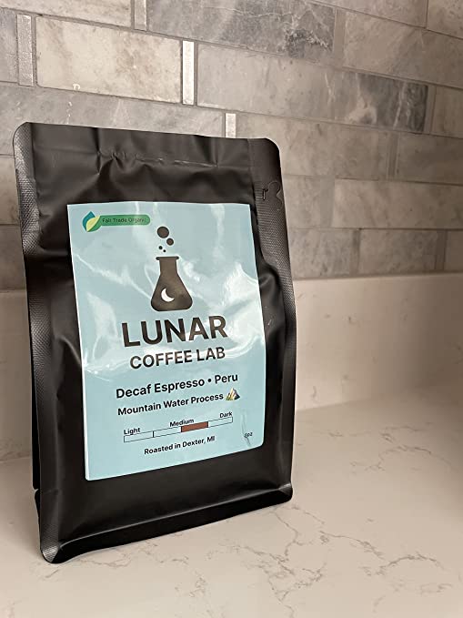 Lunar Coffee Lab Decaf Espresso Peru in a matte black pouch with a pale blue label and the moon-and-flask mark, on marble.