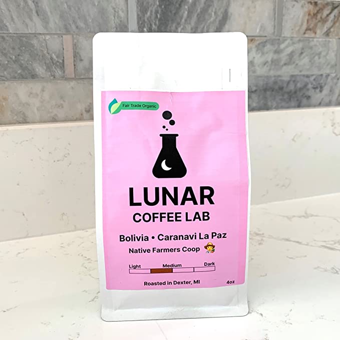 Lunar Coffee Lab Bolivia Caranavi La Paz in a white pouch with a pink label and the moon-and-flask mark, on a marble counter.