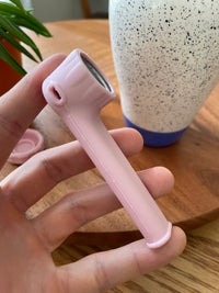 Blush silicone spoon piece held in the hand with its cap set aside, on a warm wood table.
