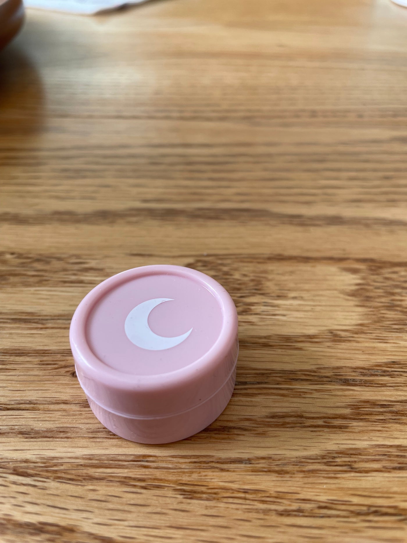 Small blush pink silicone jar with a white moon on the lid, on a warm wood table.
