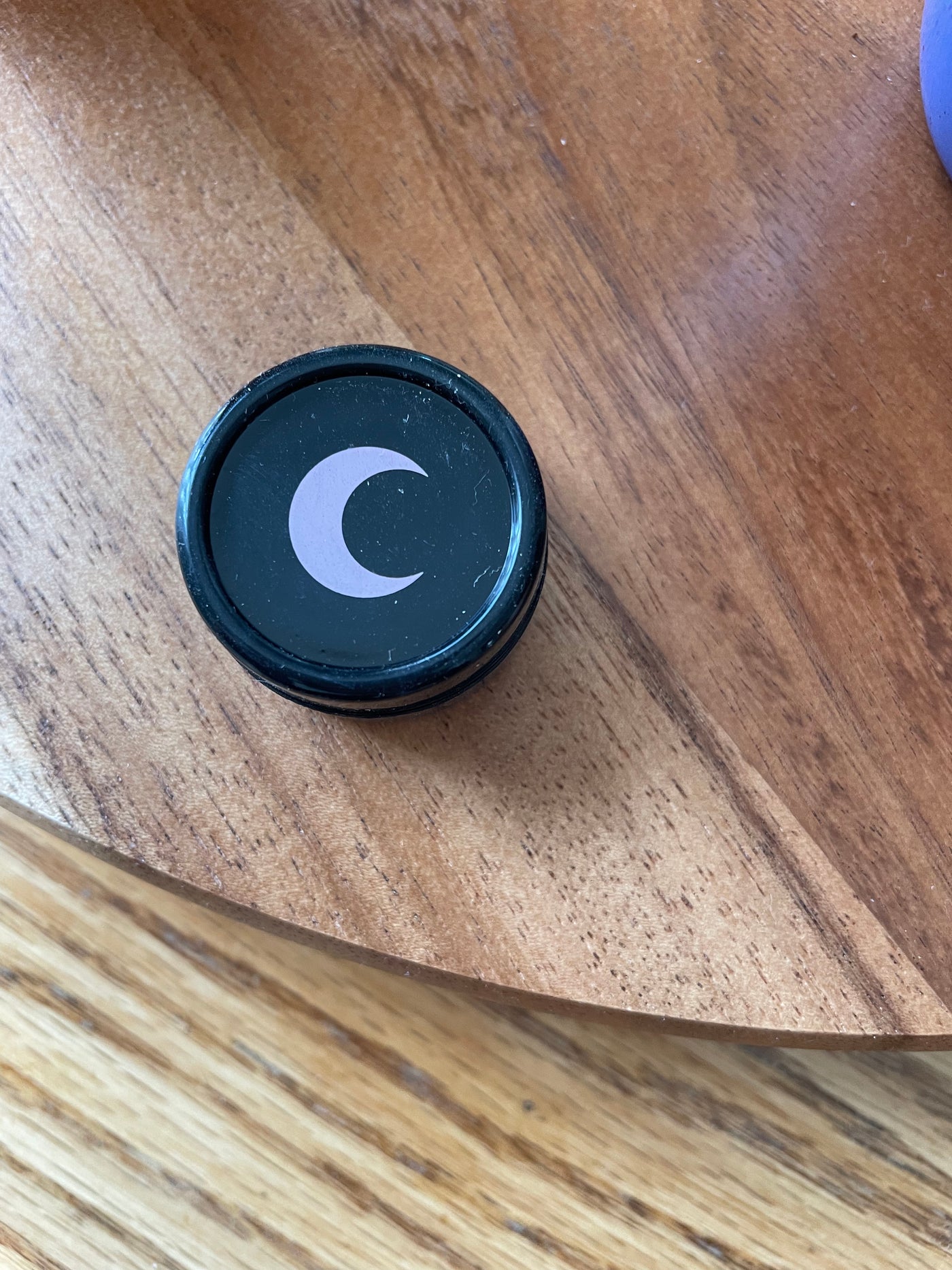 Small black silicone jar with a blush moon on the lid, seen from above on a wood table.