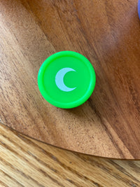 Small green silicone jar with a white moon on the lid, seen from above on a wood table.