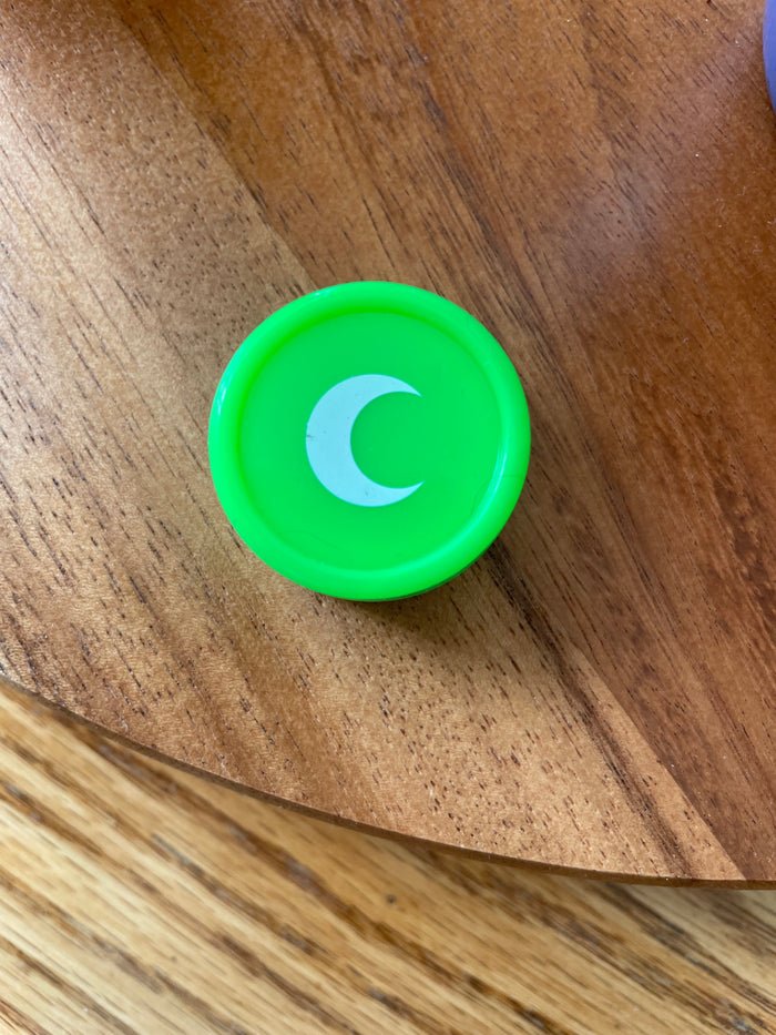 Small green silicone jar with a white moon on the lid, seen from above on a wood table.