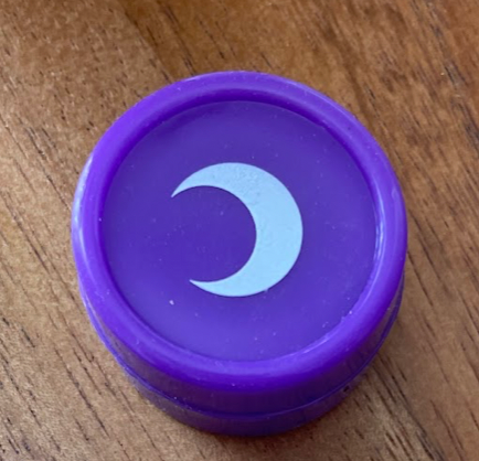 Purple silicone jar seen from above, white moon on the lid, on a wood surface.