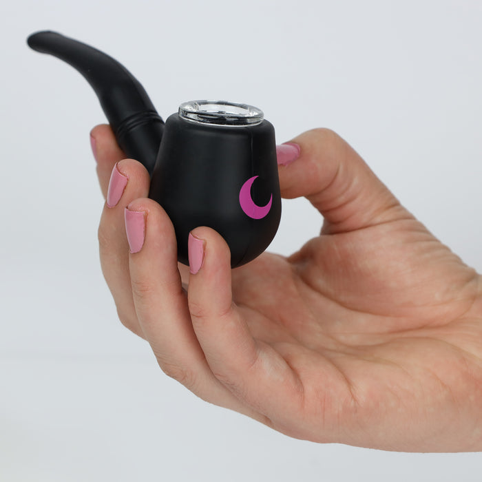 Matte black silicone tobacco-style pipe with a clear glass bowl and blush moon mark, held in a manicured hand against soft white.