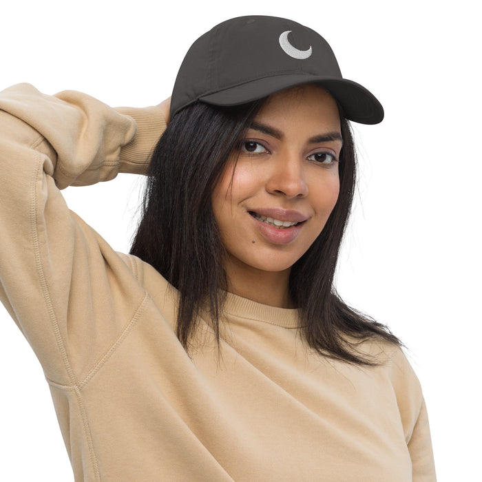 Charcoal organic baseball cap with a white crescent moon embroidered at the crown, worn with a sand sweatshirt.