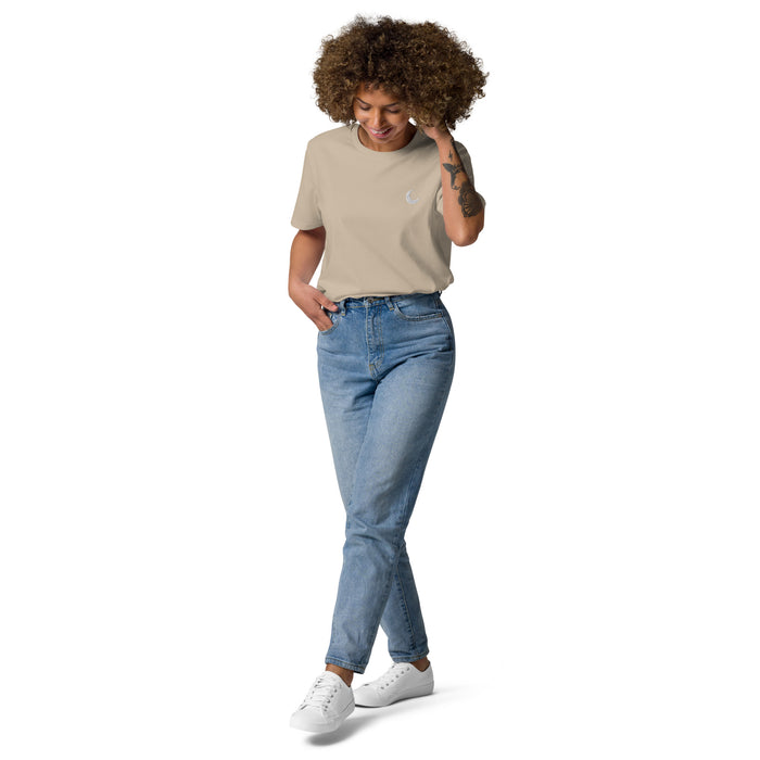 Sand-coloured organic cotton tee with a small white crescent moon at the chest, worn with light denim.