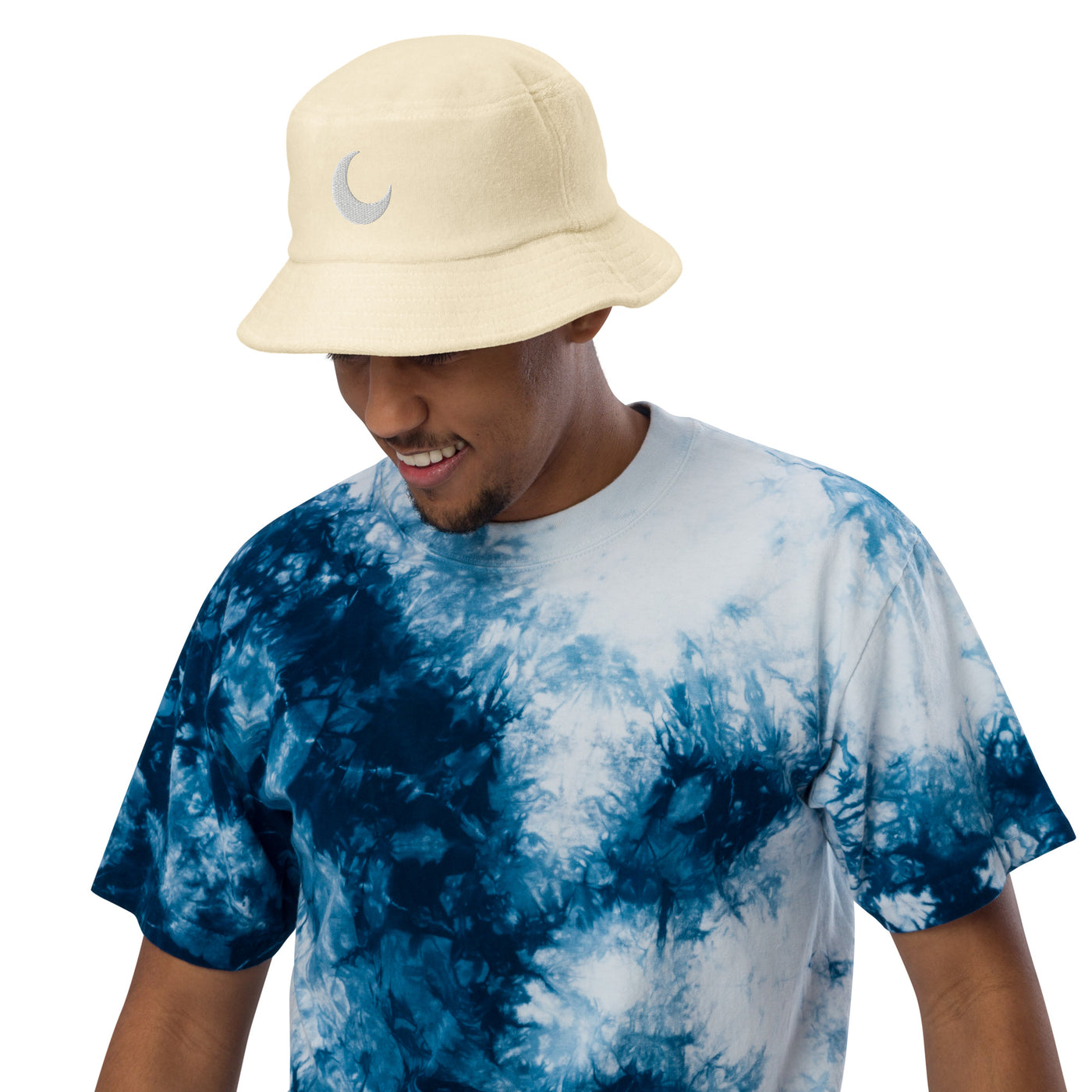 Cream terry cloth bucket hat with a white crescent moon embroidered at the front, worn with a blue tie-dye tee.